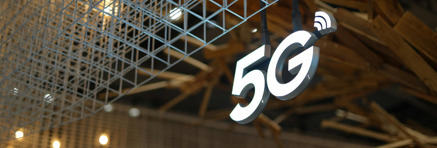 Ein leuchtendes 5G-Symbol mit WLAN-Signal hängt an einer Metallstruktur in einer modern designten Umgebung.