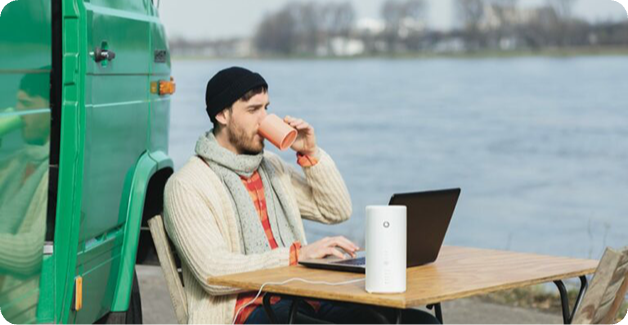 Mann trinkt Kaffee und nutzt einen Laptop mit einem LTE-Router draußen am Wohnmobil.