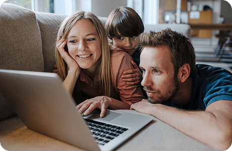 Mutter, Vater und Kind liegen auf dem Sofa und schauen gemeinsam auf einen Laptopbildschirm.