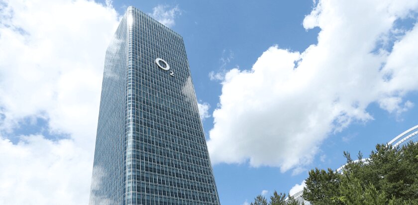 Hochhaus der Telefónica O2 in München mit reflektierender Glasfassade und blauem Himmel.